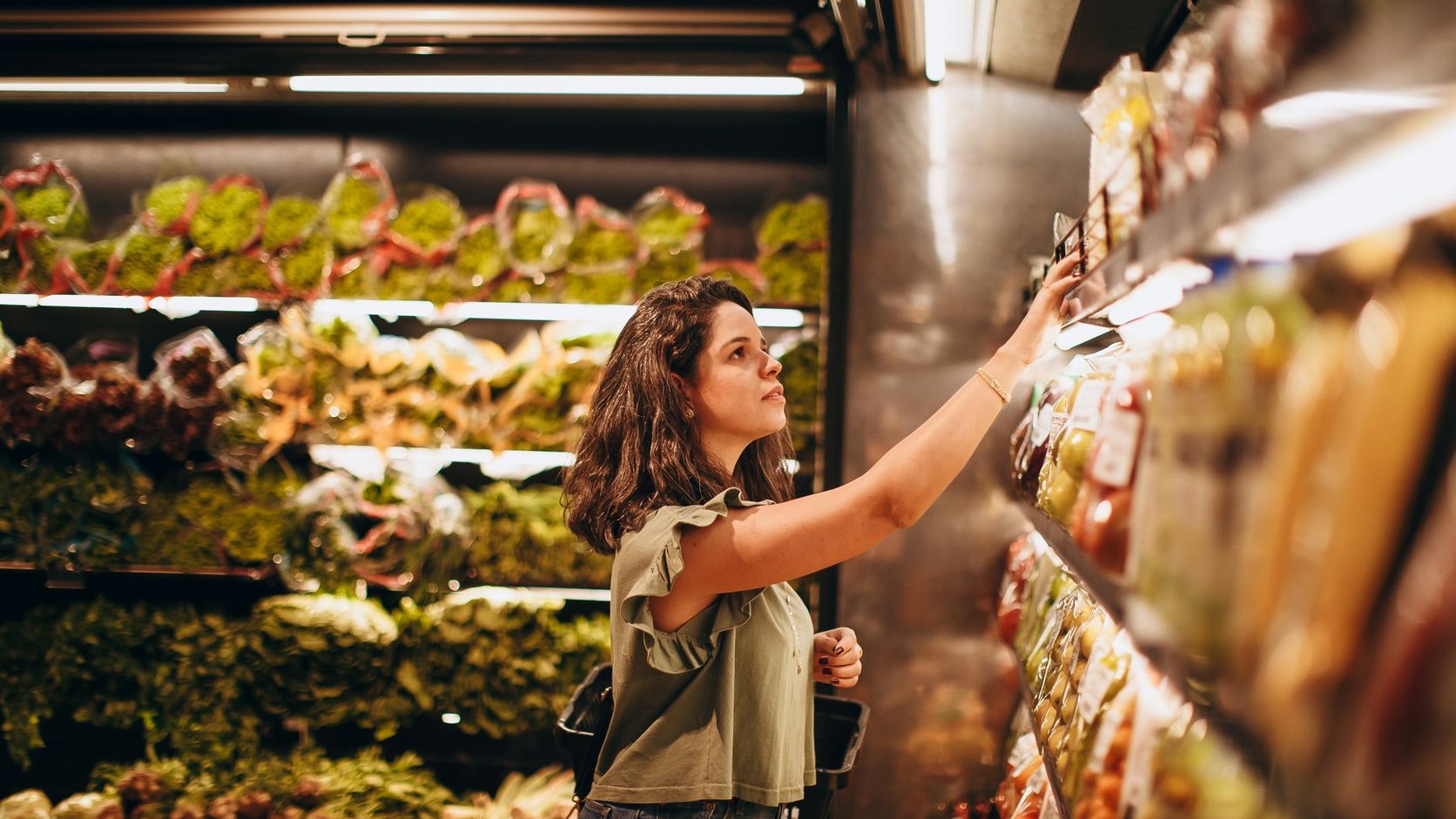 Mulher lendo rótulo de alimento na seção de hortifruti do supermercado