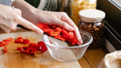Cozinheira colocando pimentão vermelho cortado em tigela de vidro na cozinha