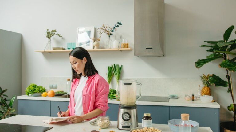 Mulher fazendo anotações na cozinha com refeição equilibrada na bancada.