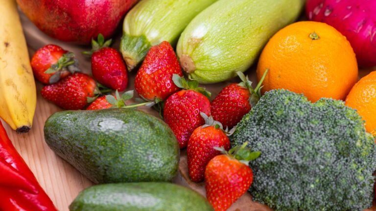 Mesa rústica com variedade colorida de frutas frescas, vegetais e alimentos ricos em fibras.