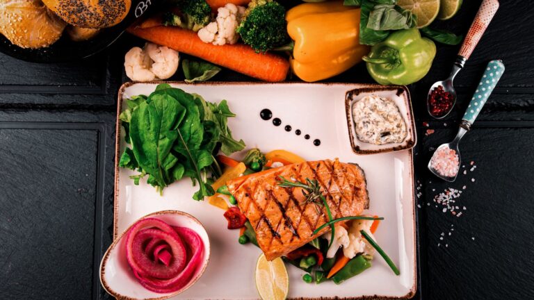 Prato saudável com salmão grelhado, vegetais variados, limão e ervas aromáticas.